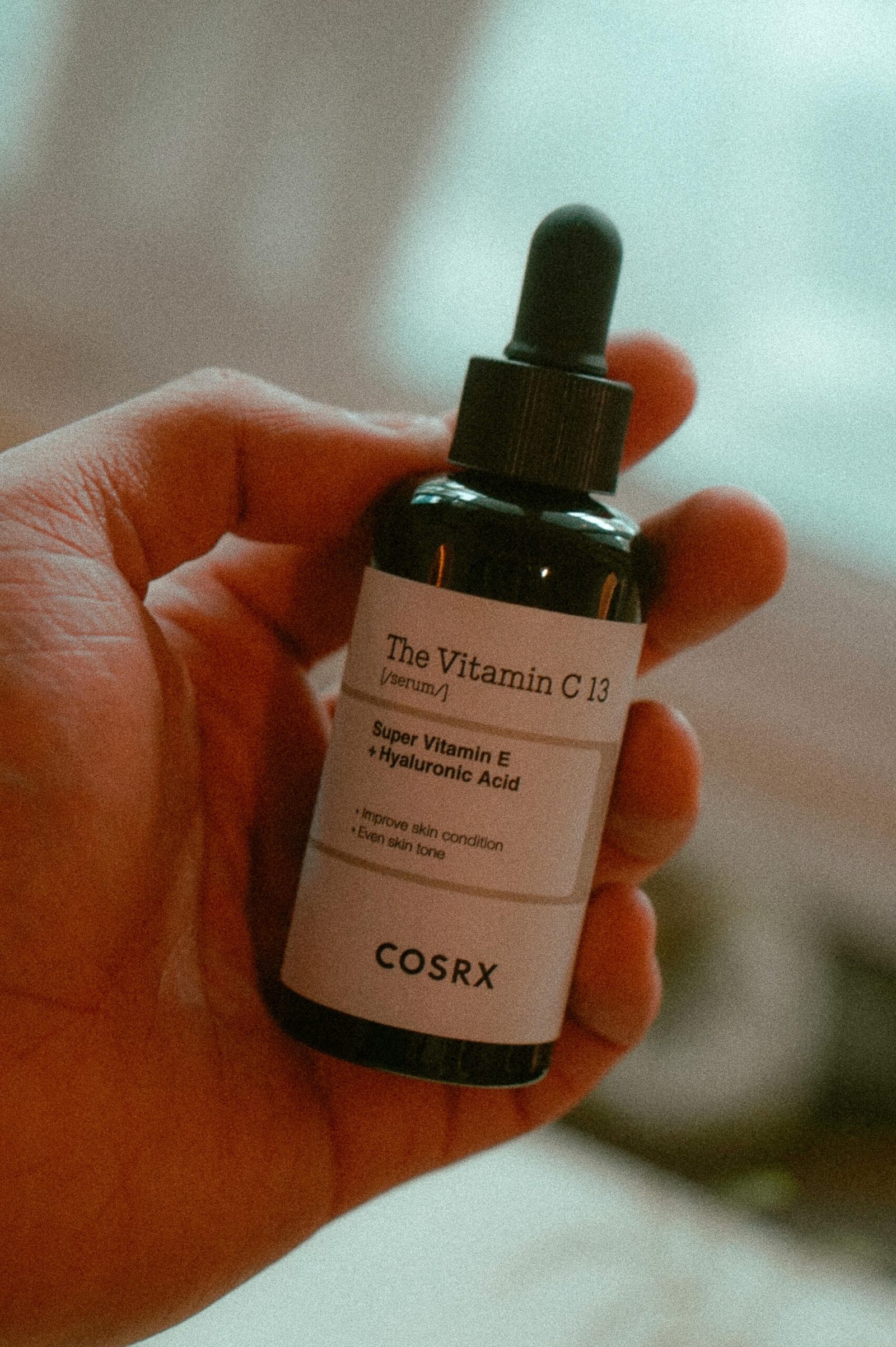Close-up of hand holding COSRX Vitamin C 13 serum bottle for skincare.