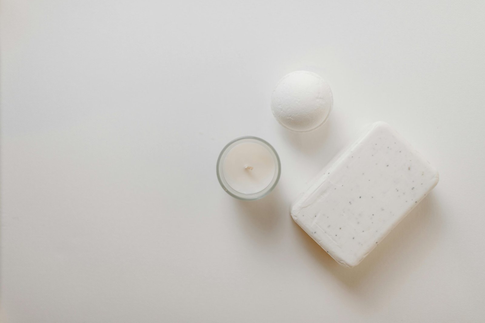 Flat lay of spa essentials, including soap, candle, and bath bomb on a white surface.
